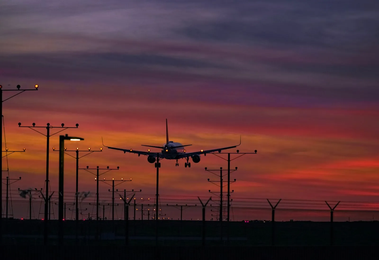 A plane coming in to land above runway approach lights at dusk.