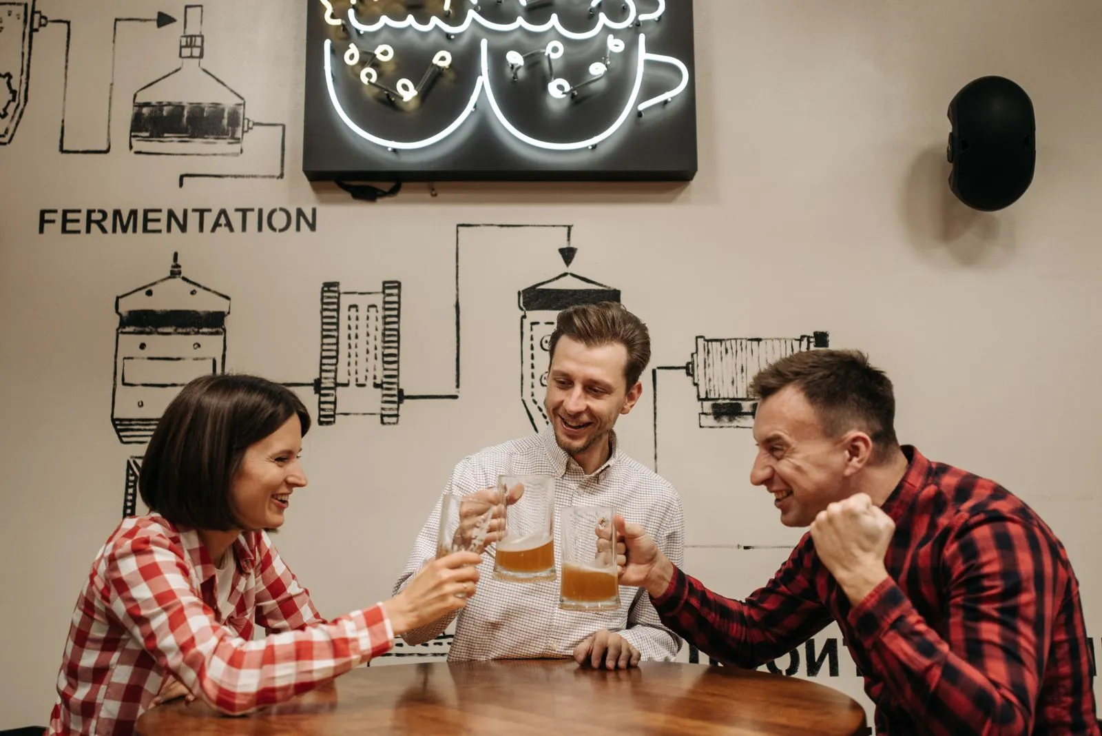 Three friends raising glasses of beer at a table in a brewery taproom.