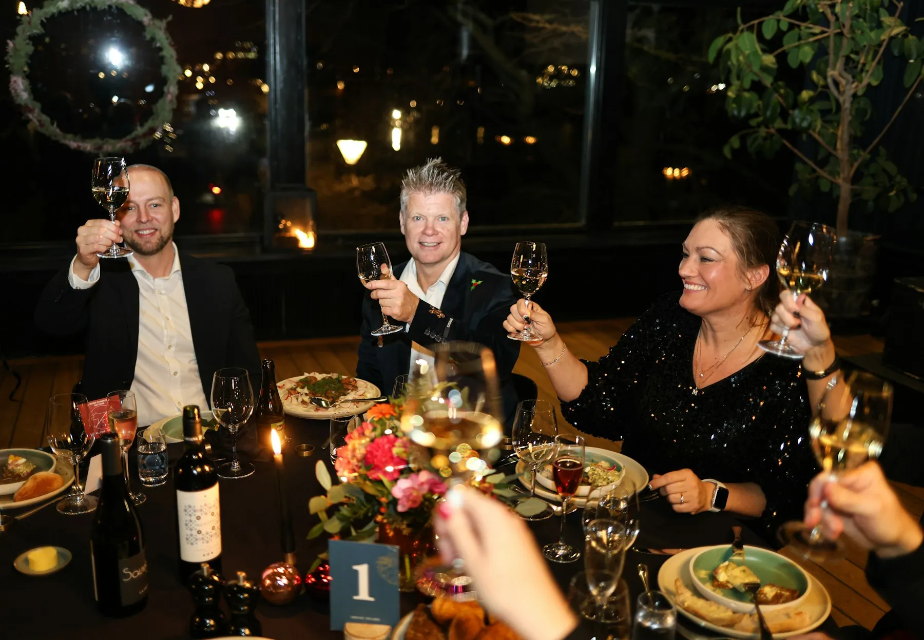 Friends raising their glasses around a candlelit dinner table.