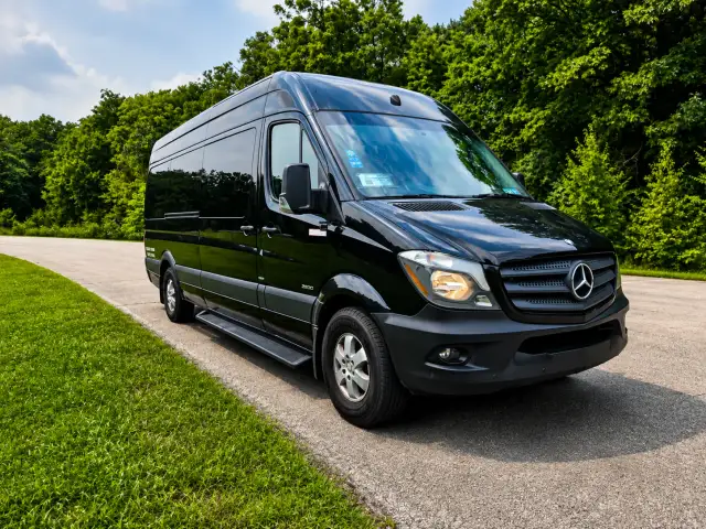 A black Executive Sprinter van on a tree-lined drive.