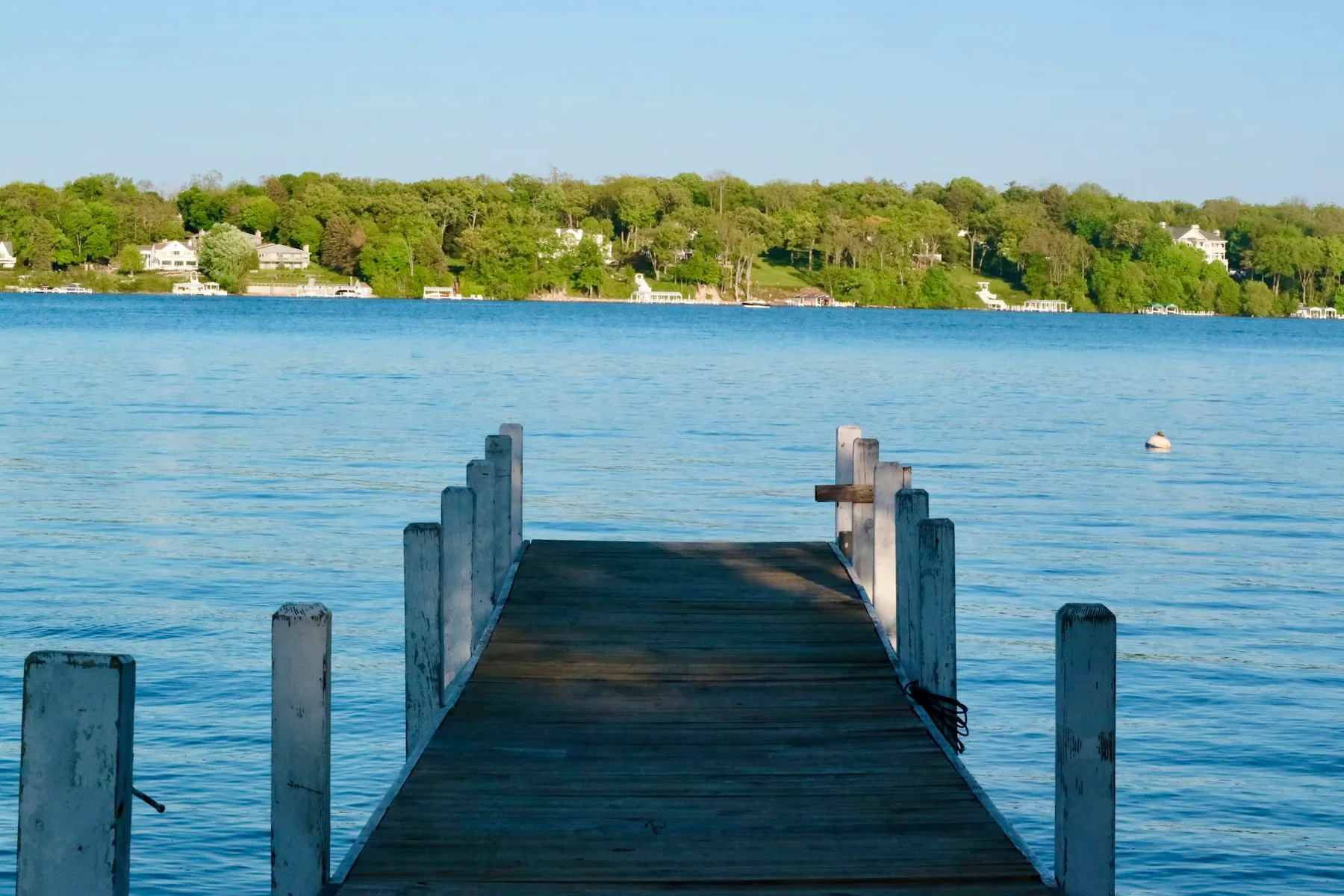 A wooden pier reaching into Geneva Lake, Wisconsin, with a leafy shoreline beyond.