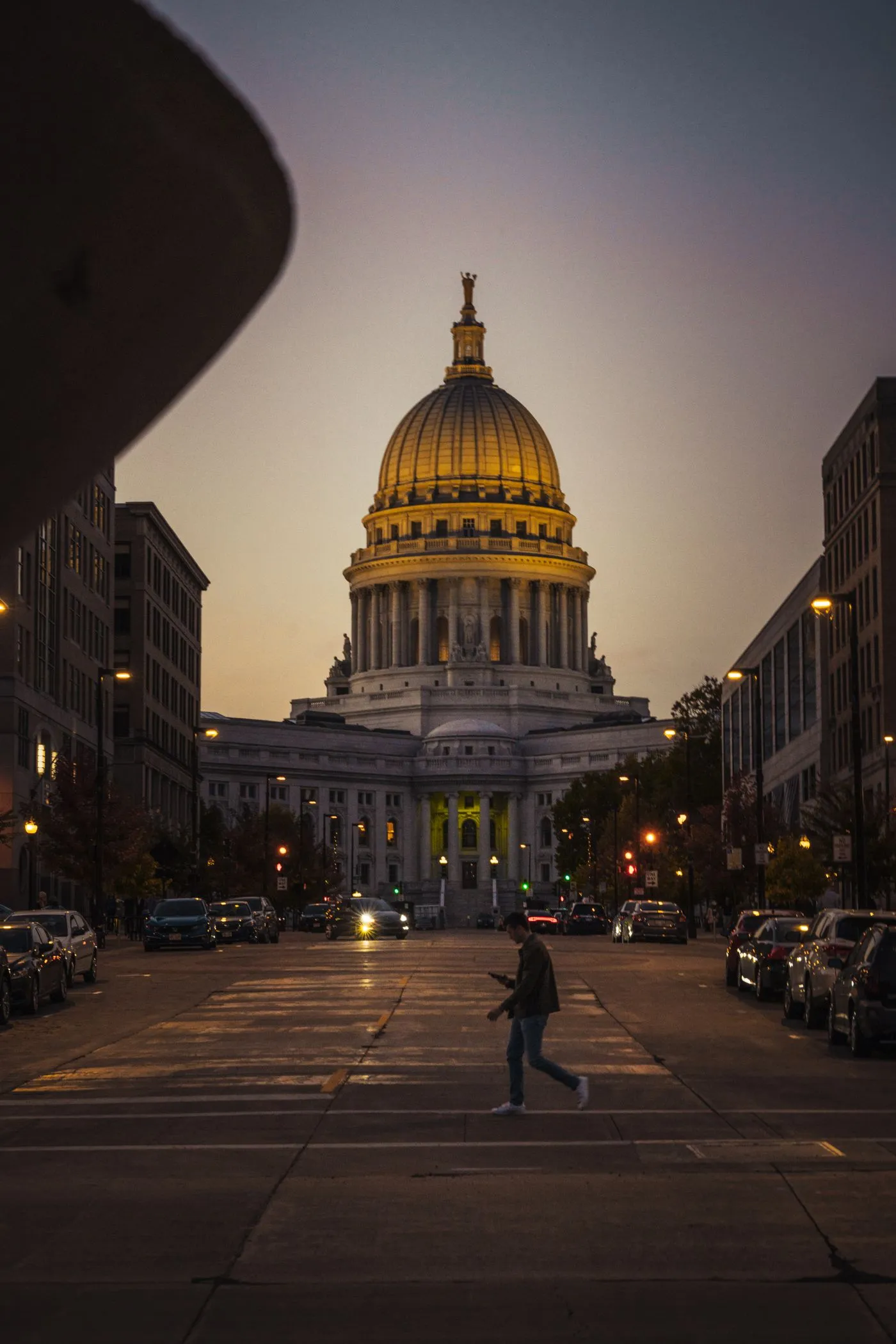 The Wisconsin State Capitol dome lit at dusk at the end of a Madison street.