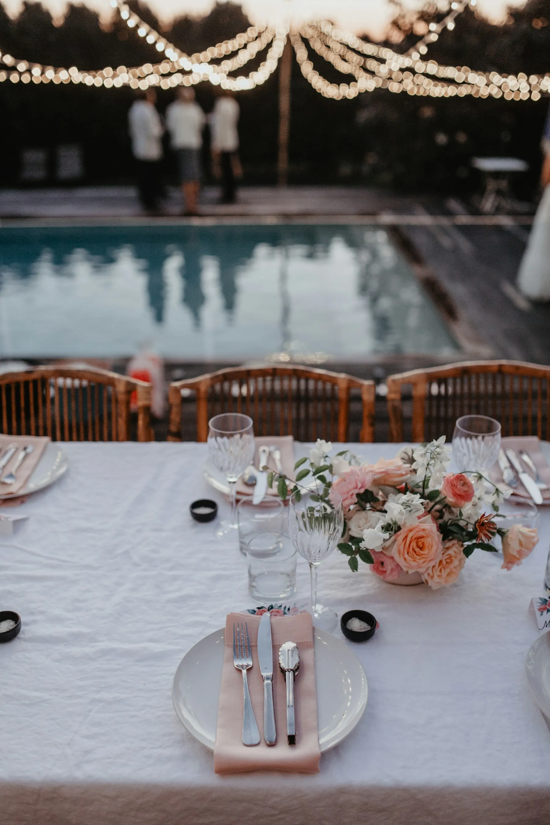 Flowers and glassware on an outdoor wedding table beneath string lights.